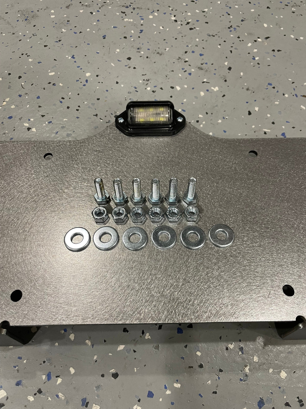 Heavy-duty steel bottom top mount license plate holder with LED light for trailers, flatbeds, RVs, and semi-trucks by Elevate Metalcraft.