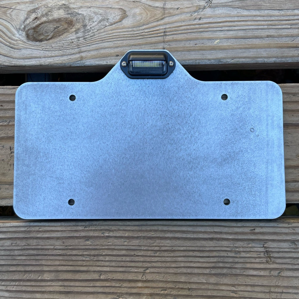 Heavy-duty steel license plate holder with LED light mounted on a flatbed trailer, suitable for RV, camper, and semi-truck.