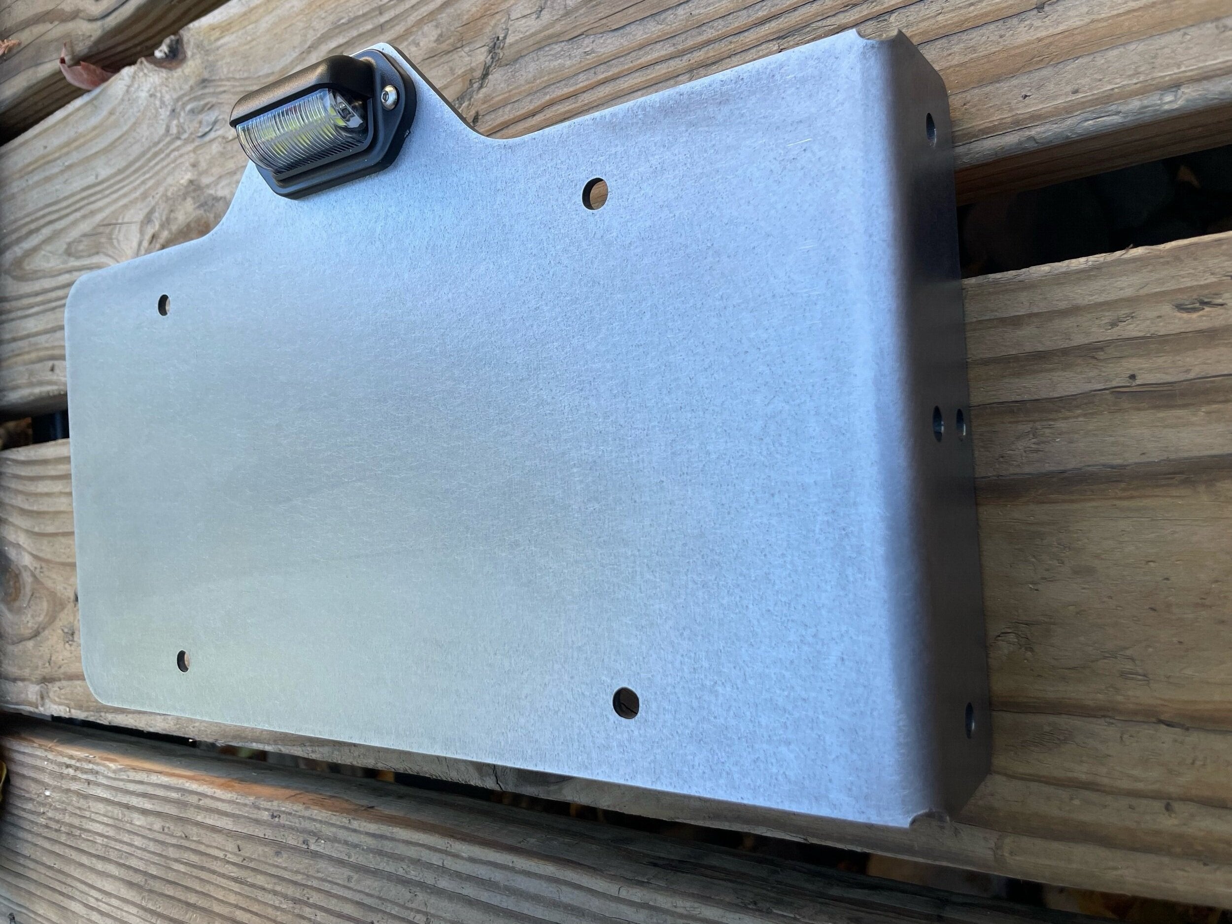 Heavy-duty steel side mount license plate holder for trailers, RVs, and semi-trailers with integrated LED light, installed on the right side.