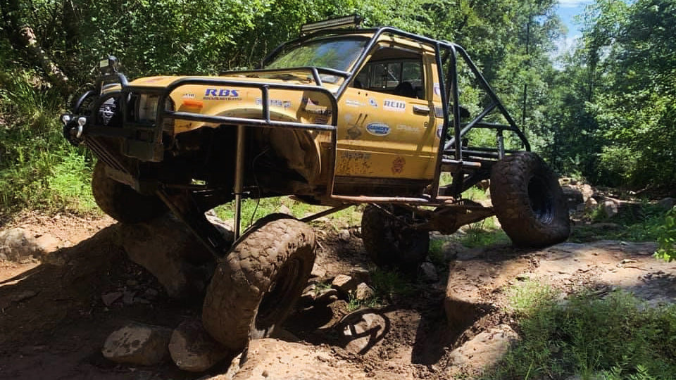 Yellow off-road vehicle on a rocky trail with trees in the background
